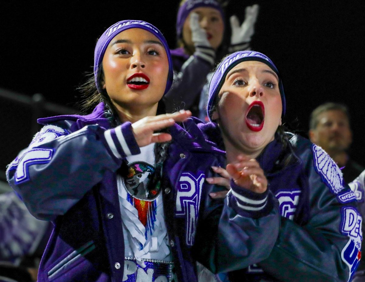 With the lead going back and forth three times in the fourth quarter, varsity twirlers Kristyn Vu ('26) and Rylee West ('26) react as the defense holds and the victory is secured, 17-14, against Midlothian Heritage in the Class 5A-II Regional round in Shenandoah on Friday, Nov. 28, 2025. The team now advances to face South Oak Cliff next week. (Ella Owens/NDN Press)
